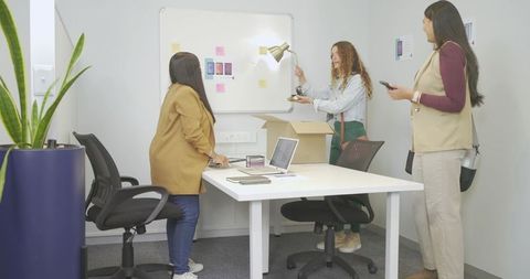 Diverse women collaborating on product mockups at whiteboard in modern small office meeting