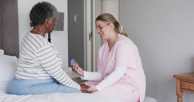 Nurse in pink scrubs providing medical assistance to elderly woman sitting on bed. Ideal for displaying compassionate healthcare services, nursing care, senior support, medical procedures, and home healthcare environments.