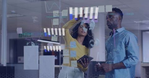Team brainstorming on glass wall with sticky notes tablet and data charts in modern office
