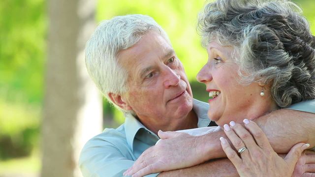 An elderly couple shares an affectionate embrace surrounded by lush greenery. The joyful expression on their faces captures a moment of tenderness and companionship, set against the serene and soothing backdrop of nature. Ideal for use in retirement living ads, healthy living brochures, or articles about lifelong love and togetherness.