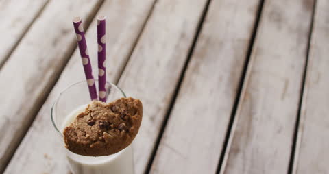 Glass of Milk with Chocolate Chip Cookie and Straws on Rustic Table