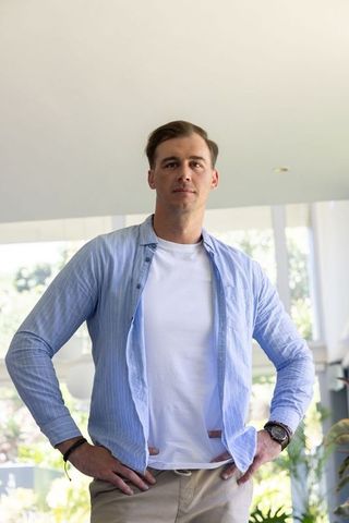 Confident man standing hands on hips in sunlit modern living room