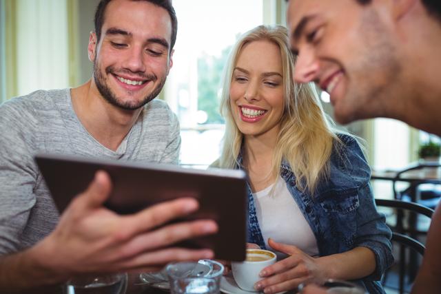 Smiling friends using digital tablet while having cup of coffee in cafÃ©