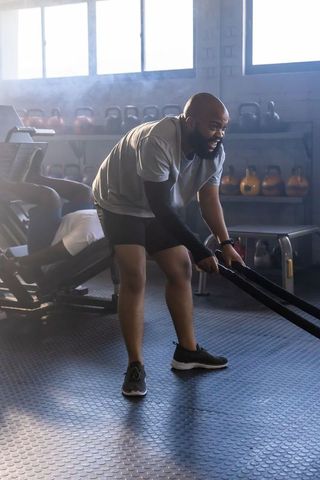 African man swinging battle ropes in industrial gym with kettlebells and focused intensity