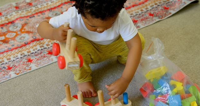 High angle view of cute little black boy playing and crouching on floor of comfortable home. He is playing with building blocks 4k