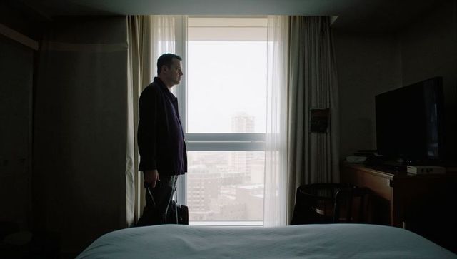 Business traveler gazing out hotel window holding rolling suitcase over city