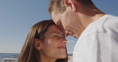 Sunlit couple touching foreheads on rocky seaside closeup romantic intimacy