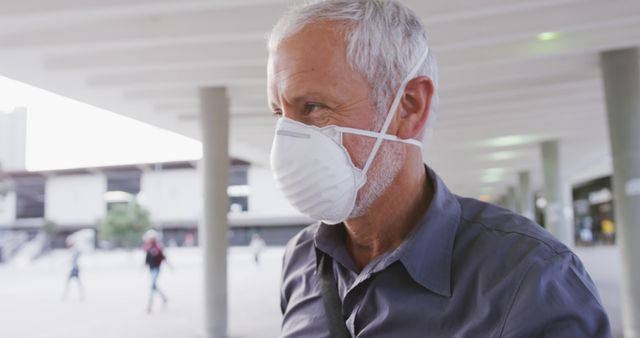 Older man wearing a face mask while walking in an urban outdoor setting. Suitable for use in health, safety, and public awareness campaigns, emphasizing the importance of wearing protective gear during pandemics or for personal safety. Useful in articles, blogs, and advertisements related to public health, aging, and community safety.