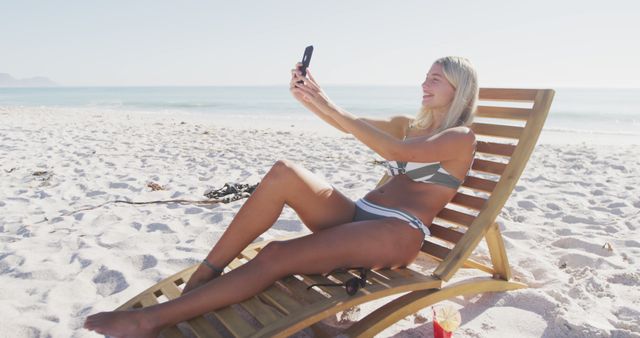 Happy caucasian woman sitting on deckchair and using smartphone on beach - Download Free Stock Photos Pikwizard.com