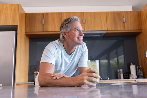 Mature man enjoying green smoothie while leaning on modern kitchen island