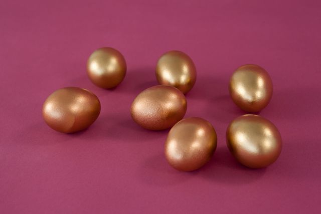 Various golden Easter eggs on pink background