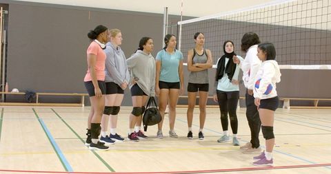Diverse female volleyball team listening to coach during indoor training