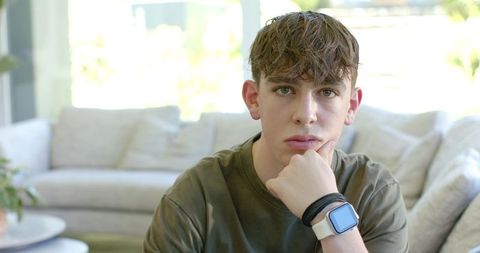 Teen resting chin on fist wearing square smartwatch in minimalist backlit living room