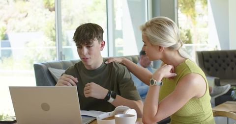 Woman mentoring teenage boy using laptop for homework and remote learning, tutor guidance