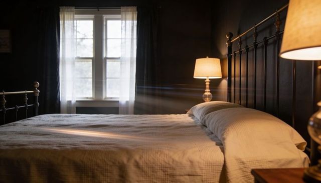 Sunlit cozy bedroom interior with metal frame bed, textured quilt, pillows and warm bedside lamps