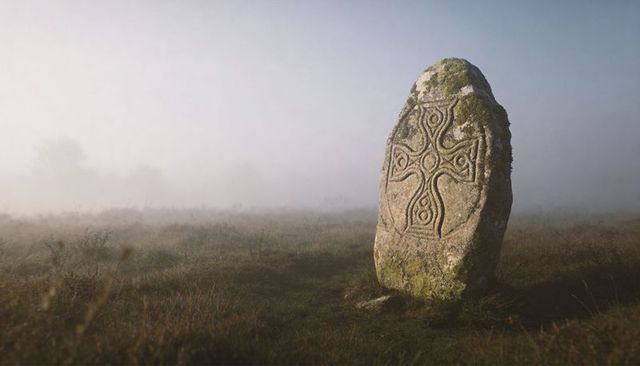 Vertical moody mist revealing ancient celtic standing stone with carved cross and moss