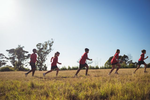 Group of children jogging together in a boot camp on a bright, sunny day. Ideal for promoting outdoor activities, fitness programs for kids, teamwork, and healthy lifestyles. Suitable for use in educational materials, fitness campaigns, and advertisements for children's sports programs.