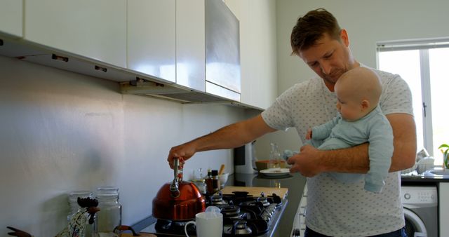 A Caucasian middle-aged man holds a baby while preparing something in the kitchen, with copy space. Balancing childcare with household tasks, he multitasks efficiently in a domestic setting.