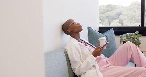 Clinician taking break on clinic sofa sipping coffee and checking phone while in scrubs