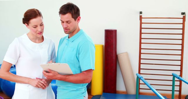 Physical therapist discussing rehabilitation plan with patient in gym setting. Ideal for use in healthcare marketing materials, websites about physiotherapy, patient education materials, and rehabilitation programs.