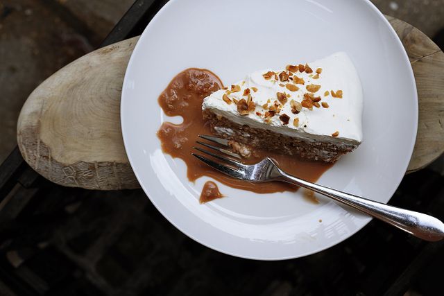 Top view of a slice of carrot cake garnished with nuts and a dollop of frosting, served on a white plate with caramel sauce on the side. The dessert is presented with a fork rests on the plate. Suitable for use in food blogs, restaurant menus, or gourmet recipe collections.