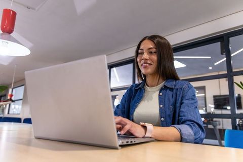 Young woman working on laptop in modern coworking space with glass walls and smartwatch