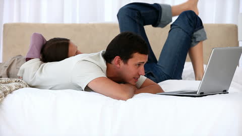 Couple Relaxing Together on Bed While Working on Laptop