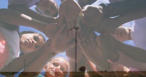 Children Joining Hands in Circle Overlaid with Wind Turbines Symbolizing Clean Energy Teamwork