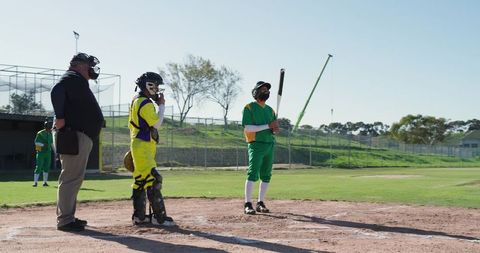 Batter Waiting at Home Plate with Catcher and Umpire Standing on Sunny Baseball Field
