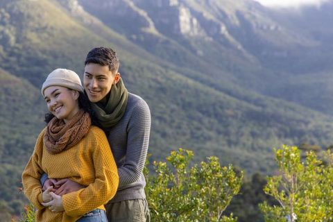 Asian couple embracing on mountain overlook wearing knit sweaters and scarves, fall scene
