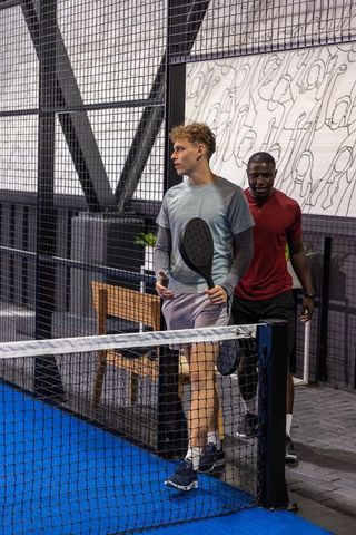 Young diverse players walking on indoor padel court holding paddles after match