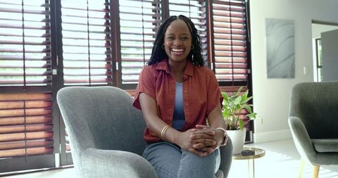 Smiling woman sitting in modern living room clasping hands wearing rust shirt and jeans