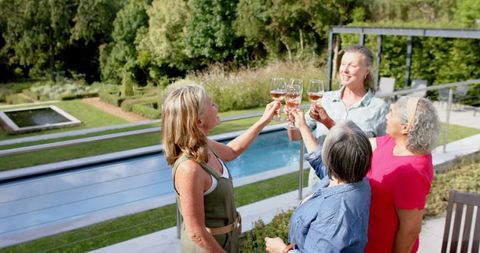 Senior Women Enjoying Wine and Laughter by Pool on Sunny Day