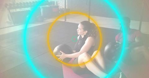 Woman twisting with medicine ball for core workout on mat with partner, neon circle overlay