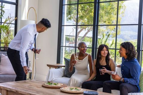 Diverse friends enjoying cocktail gathering in bright modern living room with pizza