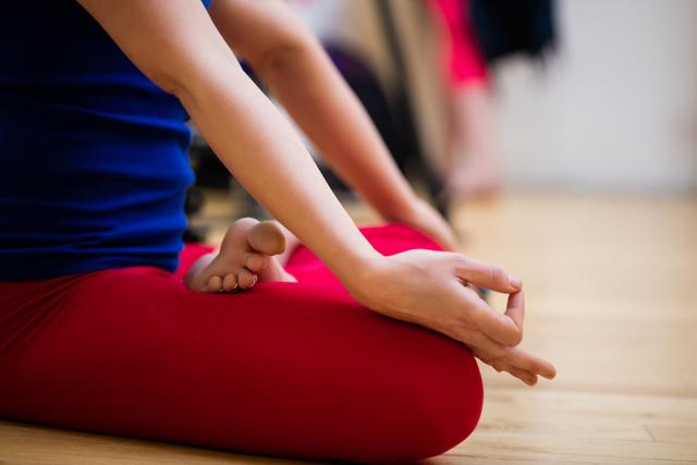 Woman sitting in lotus position on wooden floor in fitness studio. Ideal for promoting yoga classes, mindfulness workshops, wellness retreats, and healthy lifestyle content. Can be used in articles about mental health, relaxation techniques, and physical fitness.