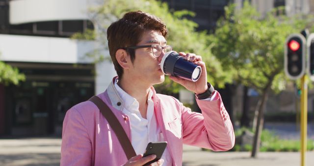 Asian man drinking coffee and using smartphone while crossing the street. business and lifestyle concept
