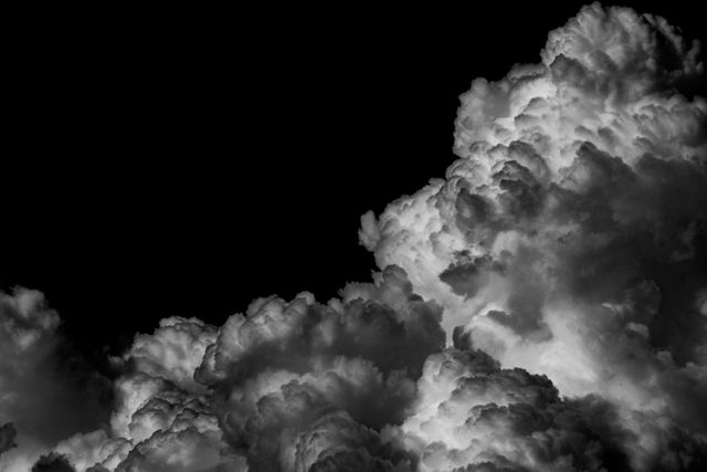 Dramatic storm clouds appear striking in black and white, presenting a powerful and ominous scene. Highlighting the textures and shapes of towering clouds, this image can be used for weather-related content, dramatic or ominous settings, mood backgrounds, or nature and photography blogs.
