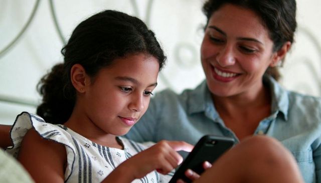 Mother and daughter sharing smartphone bonding moment on bed, smiling parent watching