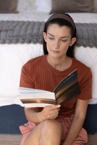 Mid-adult woman reading paperback on bedroom floor, cozy calm moment in natural light