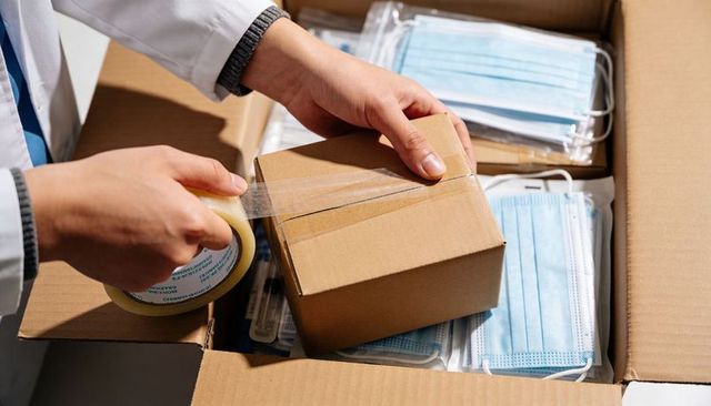 Healthcare worker sealing cardboard box while packing surgical masks for safe delivery