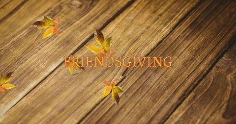 Friendsgiving golden lettering on rustic wood planks with autumn leaves and warm tones