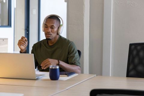 Focused african american man wearing headphones working on laptop in modern coworking space