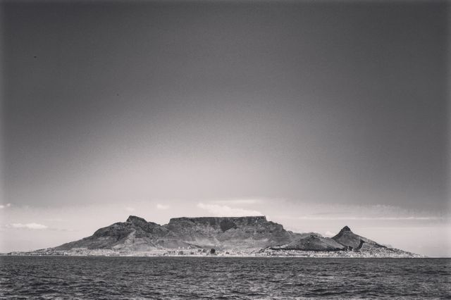 Monochrome landscape of Table Mountain viewed from the sea under a clear sky. Ideal for use in travel promotions, photography showcases, wall art, and tourism marketing materials highlighting Cape Town, South Africa. The dramatic black and white filter adds a timeless, classic appeal.