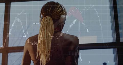 Woman with braids tracking stock market charts on window while wearing headset