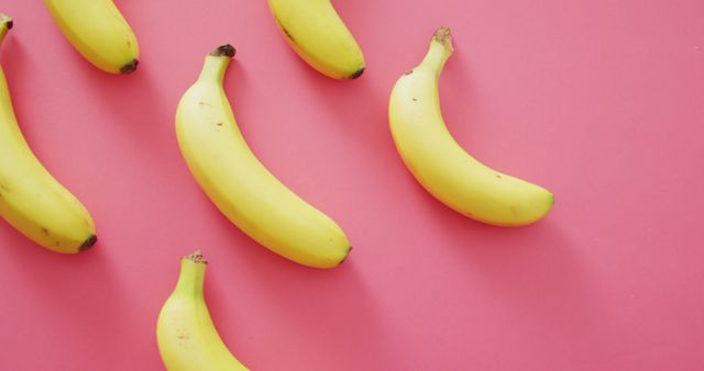 Several fresh yellow bananas lie on a striking pink background, creating a vivid and lively contrast. The bananas appear ripe and ready to eat, emphasizing healthy eating and nutrition themes. This dynamic image can be used in marketing materials for grocery stores, health and wellness content, food blogs, and tropical themed promotions.