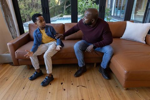 African american father and preteen son having serious talk on leather sofa near pool