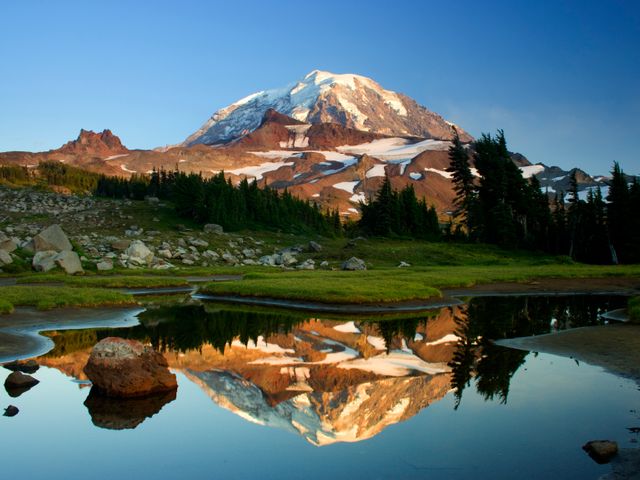 This image features a majestic snowcapped mountain reflected perfectly in an alpine lake surrounded by lush greenery and rocky terrain. Ideal for use in travel brochures, nature documentaries, environmental campaigns, and outdoor adventure promotions. The serene and picturesque setting evokes feelings of tranquility and awe, perfect for inspiring travel enthusiasts and nature lovers.