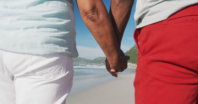 Couple enjoys romantic walk hand in hand on beach. Ideal for depicting love, companionship, travel enjoyment. Useful in articles or promotions focused on relationships, beach vacations, senior lifestyle.