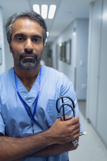 Portrait of biracial male doctor standing with arms crossed in the corridor at hospital